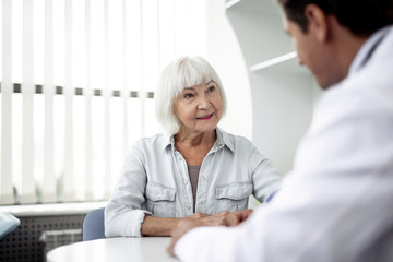 Wall Mural - Calm elderly lady sitting in front of her practitioner and feeling interested while talking to him and smiling