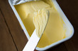 Whipped butter in plastic container with knife, butter for cooking and sandwiches. Rustic wooden table.
