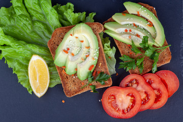 Close-up of sliced avocado toasts and tomato on dark background