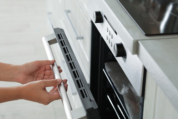 Wall Mural - Young woman opening electric oven in kitchen, closeup