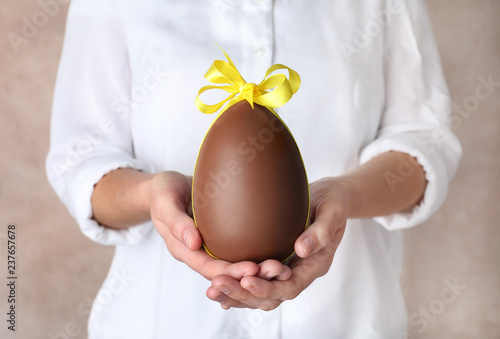 Plakat Woman holding chocolate Easter egg with bow knot on color background, closeup