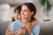© fizkes - Head shot portrait smiling attractive female sitting embracing with little adorable daughter on couch in living room at home looking away. Happy motherhood new mother for adopted child concept