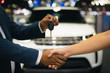 Handshake of two businessmen when selling a car in a motor show, auto business, car sale, deal, gesture and people concept - close up of dealer giving key to new owner and shaking hands in showroom.