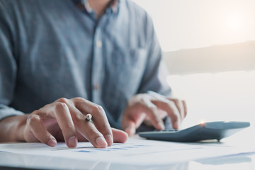 Close up of businessman or accountant hand holding pen working on calculator to calculate business data, accountancy document and laptop computer at office, business concept