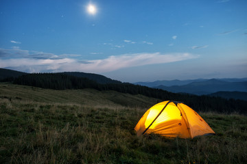 Wall Mural - illuminated orange tent in mountains at dusk