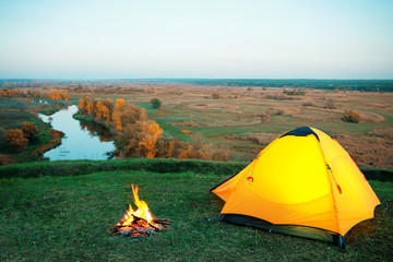 Wall Mural - orange lighted tent and campfire on hill above the river