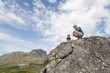 © Connect Images - Boy and father crouching on top of rock formation, low angle view, Oppland, Nord-Trondelag, Norway