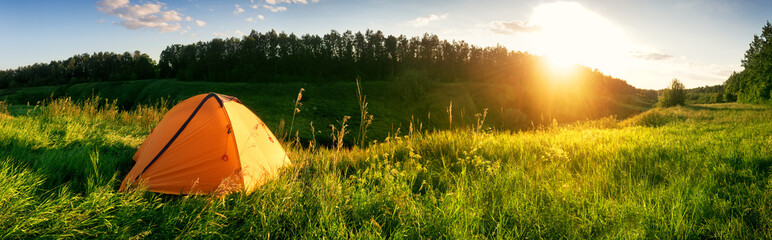 Wall Mural - orange tent in the mountains on a green meadow