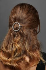 Close up isolated portrait of a young lady with brown ombre hair colour. The back view of the girl with half-up hairstyle, adorned with silver O-ring barrette. Posing against the grey background.