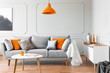 © Photographee.eu - Orange lamp above table and grey settee with cushions in bright flat interior with poster. Real photo