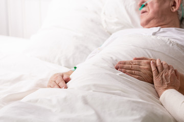 Wall Mural - Senior man with terminal illness laying in hospital bed, helping and on his hand as symbol of support, photo with copy space