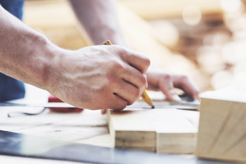 A carpenter in working clothes and a small business owner takes a wooden board with a ruler and pencil.