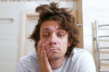 sleepy shaggy young man looks at the mirror in bathroom in the morning.