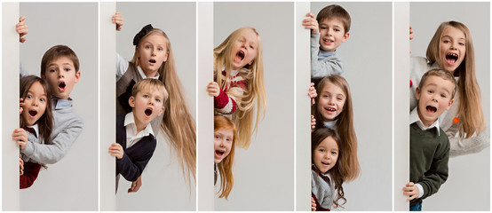 Wall Mural - Banner with a surprised children peeking at the edge with copyspace. The portrait of cute little kids boy and girls looking at camera against white studio wall. Kids fashion and happy emotions concept