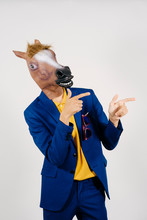 Unrecognizable Man Disguised With A Horse Head And Dressed With A Blue Suit Posing In A Studio Set