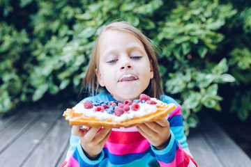 waffles - girl eating a waffle with whipped cream, raspberries and blueberries outdoors  in the garden smiling