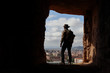 EXPLORER WITH AUSTRALIAN HAT AND BACKPACK OBSERVING THE CITY FROM A HIGH CAVE