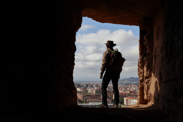explorer with australian hat and backpack observing the city from a high cave