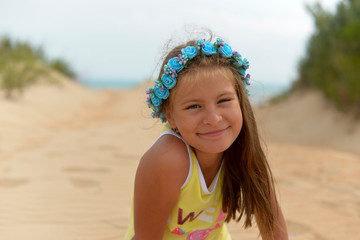 Wall Mural - Teenage girl in a flower wreath on her head sitting on the Golden sand on the beach in the summer