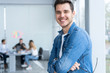 © opolja - Smiling businessman in denim shirt looking at camera in office.
