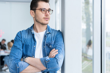 Wall Mural - Smiling businessman in denim shirt and eyeglasses looking at camera in office.