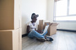 © F8  \ Suport Ukraine - Attractive African American woman unpacking boxes in her new home sitting on the floor with laptop in the living room