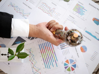 Wall Mural - top view hand of businessman hold light bulb with coin and calculator on business graph. concept of 