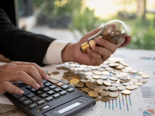 Wall Mural - hands of businessman holding a light bulb with coin. the idea of ​​reducing costs and reduce energy 