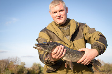 Happy fisherman with large pike fish a trophy. Fisherman shows a fish.