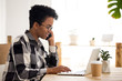 © fizkes - Busy black girl wearing glasses talk on smartphone working at laptop at wooden desk, smiling African American woman speak on cell using computer, happy afro female have phone conversation in office