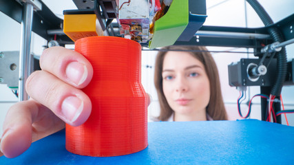 Canvas Print - Young women designer in 3d printing lab. Girl takes the finished detail from 3D printer