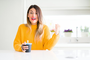 Young beautiful woman drinking a cup of coffee at home screaming proud and celebrating victory and success very excited, cheering emotion