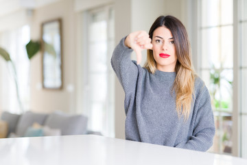 Poster - Young beautiful woman wearing winter sweater at home looking unhappy and angry showing rejection and negative with thumbs down gesture. Bad expression.