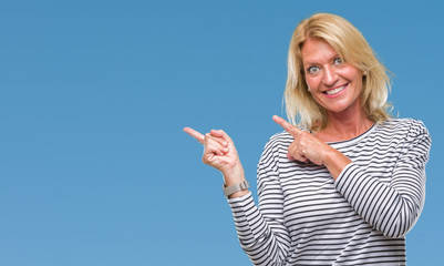 Middle age blonde woman over isolated background smiling and looking at the camera pointing with two hands and fingers to the side.