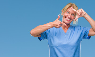 Canvas Print - Middle age blonde woman wearing doctor nurse uniform over isolated background smiling making frame with hands and fingers with happy face. Creativity and photography concept.