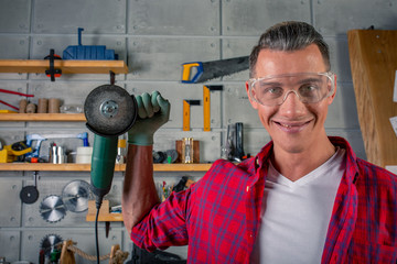 young handsome smiling caucasian carpenter holding a circular saw in his hands in the workshop. Ready to work