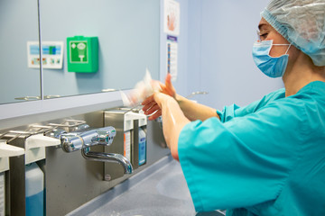 Female Surgeon in a medical mask and in a suit in the hospital washing thoroughly her hands before performing a surgery