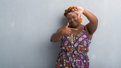 Canvas Print - Young african american woman over grey grunge wall wearing orange braids smiling making frame with hands and fingers with happy face. Creativity and photography concept.