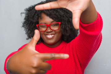 Poster - Young african american plus size woman over grey grunge wall wearing winter sweater smiling making frame with hands and fingers with happy face. Creativity and photography concept.