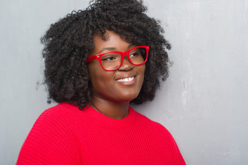 Poster - Young african american plus size woman over grey grunge wall wearing winter sweater looking away to side with smile on face, natural expression. Laughing confident.