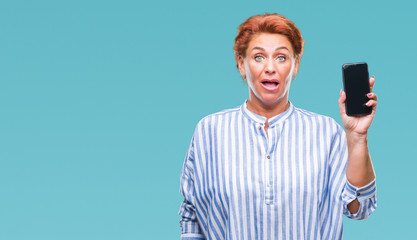 Sticker - Atrractive senior caucasian redhead woman showing smartphone screen over isolated background scared in shock with a surprise face, afraid and excited with fear expression