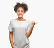 © Krakenimages.com - Young afro american woman over isolated background smiling with happy face looking and pointing to the side with thumb up.