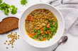 Homemade vegan lentil soup with vegetables, bread and cilantro, white wooden background.