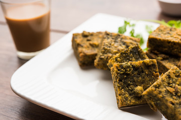 A savory cilantro cake or kothimbir vadi in square shape which is first steamed and then fried until crisp. popular indian snack served with hot tea and tomato ketchup