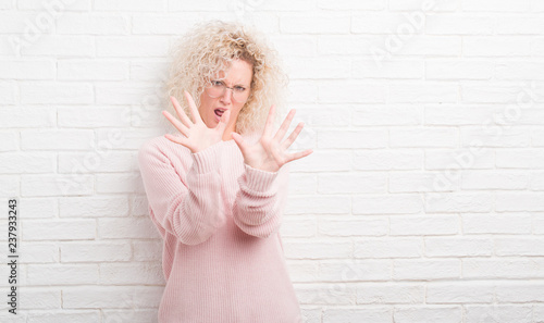 Young Blonde Woman With Curly Hair Over White Brick Wall Afraid