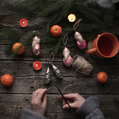 Vintage christmas toy on wooden vintage background. The hands of a woman cut the thread to hang the ornament on the spruce. Festive mood, tangerines, candles. The concept of celebrating Christmas in t