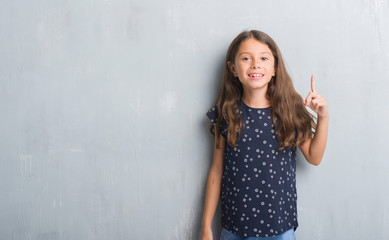 Sticker - Young hispanic kid over grunge grey wall showing and pointing up with finger number one while smiling confident and happy.