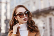 Outdoor close up portrait of young beautiful woman wearing trendy leopard print sunglasses, hoop earrings,  white turtleneck, coat, model posing in street of european city. Copy, empty space for text