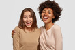 © WHstudio Leushin N - Photo of joyful ladies embrace and enjoy togetherness, being of different of races, dressed in casual jumpers, isolated over white background. Diverse women laugh happily, have fun together.
