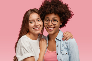 Wall Mural - Portrait of friendly multiethnic women smile broadly, cuddle and enjoy togetherness, pose for family portrait, wear casual clothes, isolated over pink background. Ethnicity and friendship concept